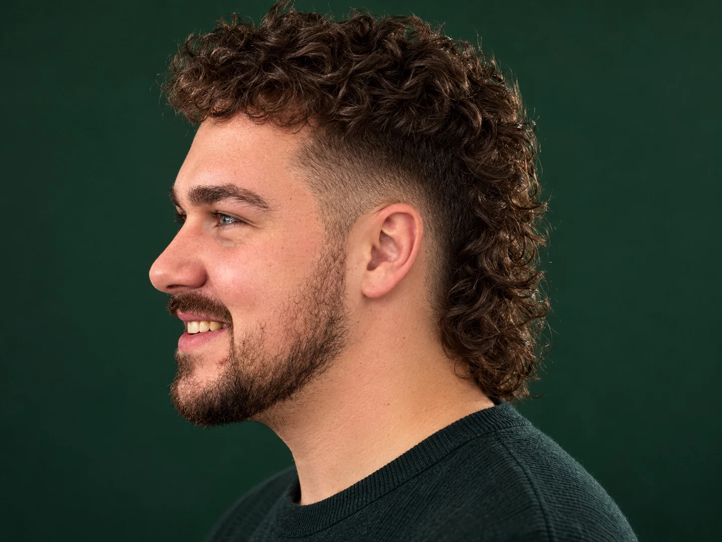 Man met een moderne mullet met een burst fade rond zijn oor en langer haar in de nek, van opzij gezien