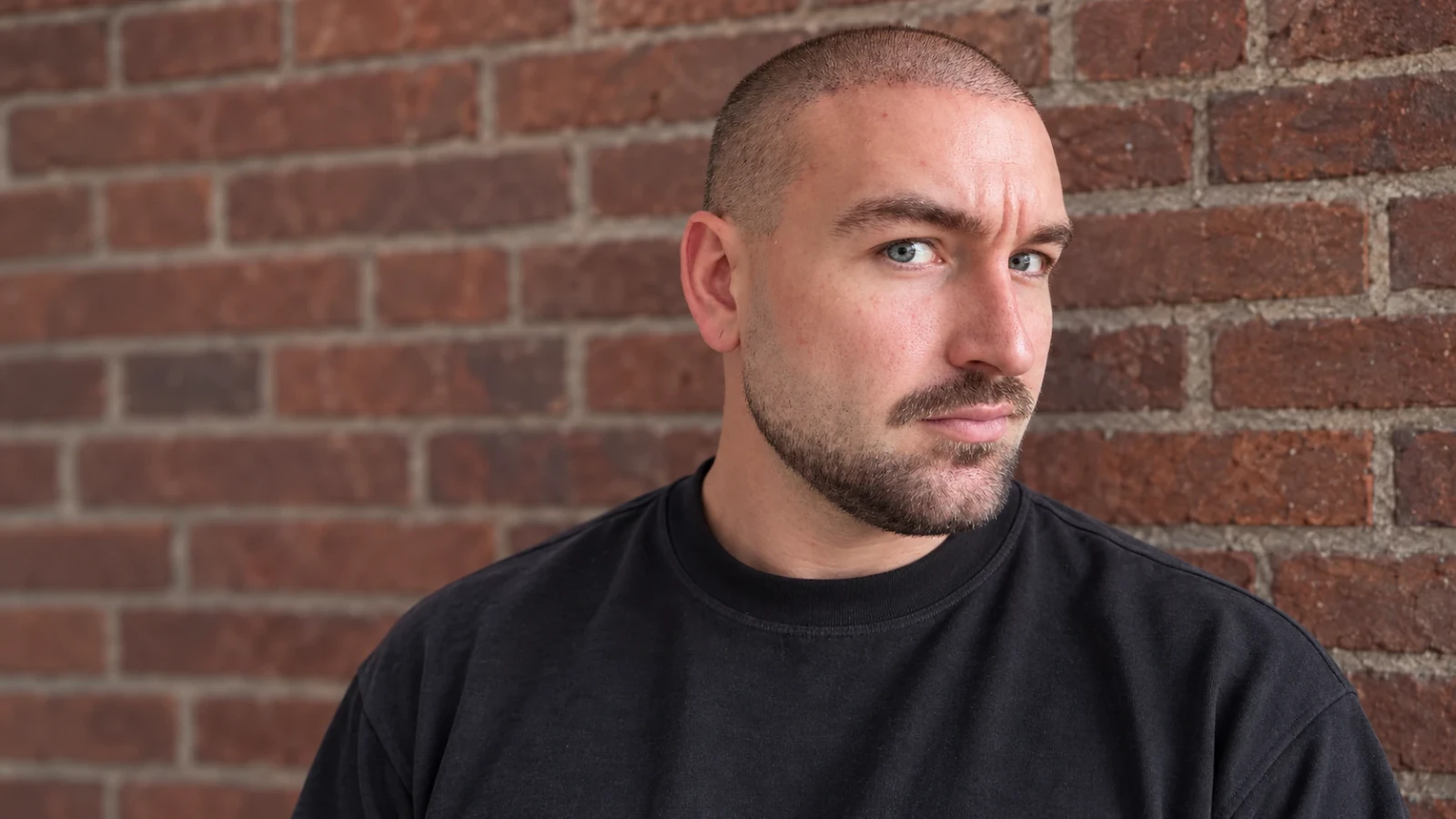 Man met een korte buzz cut en een verzorgde baard voor een bakstenen muur