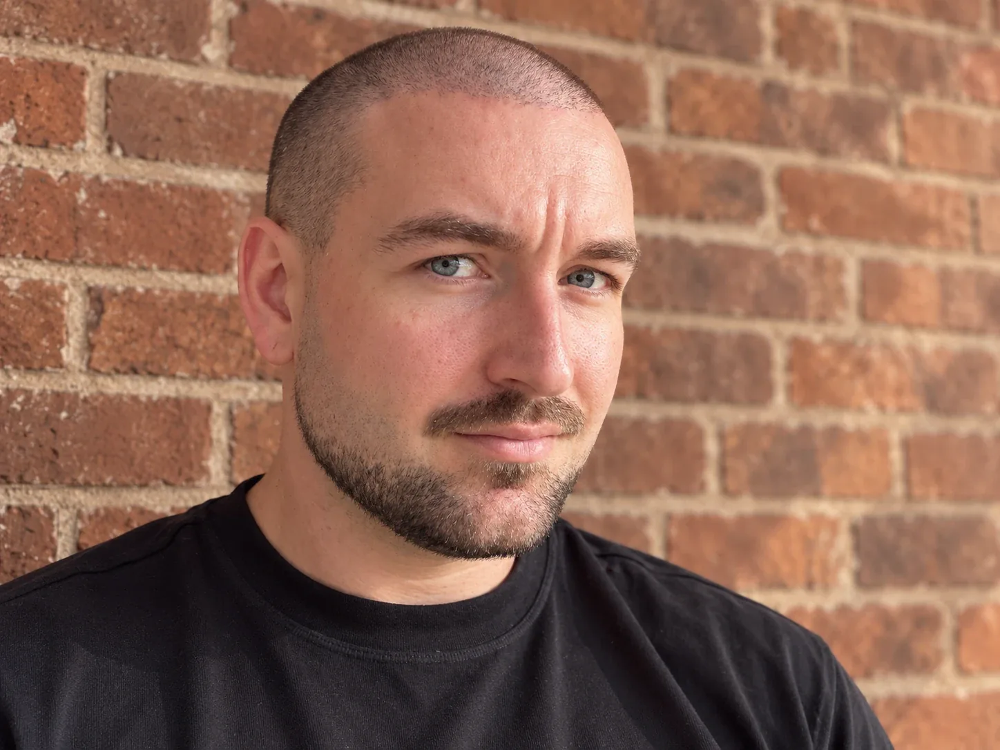 Man met een korte buzz cut en een verzorgde baard voor een bakstenen muur