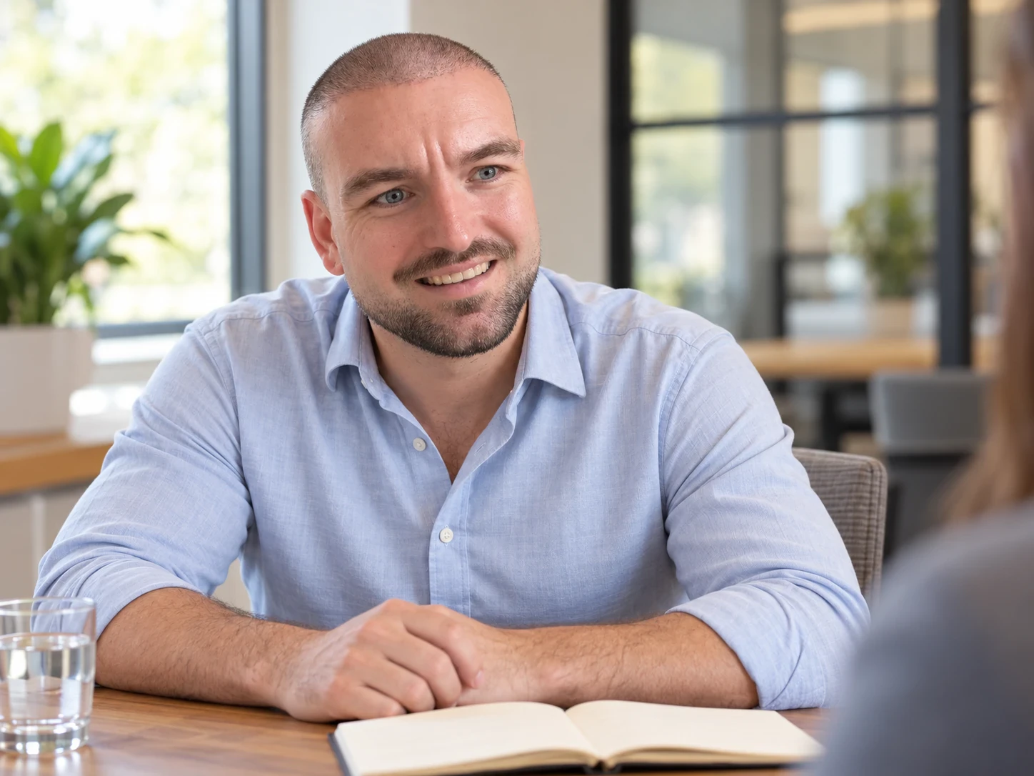 Man met een buzz cut en een korte, verzorgde baard in een overhemd aan een vergadertafel